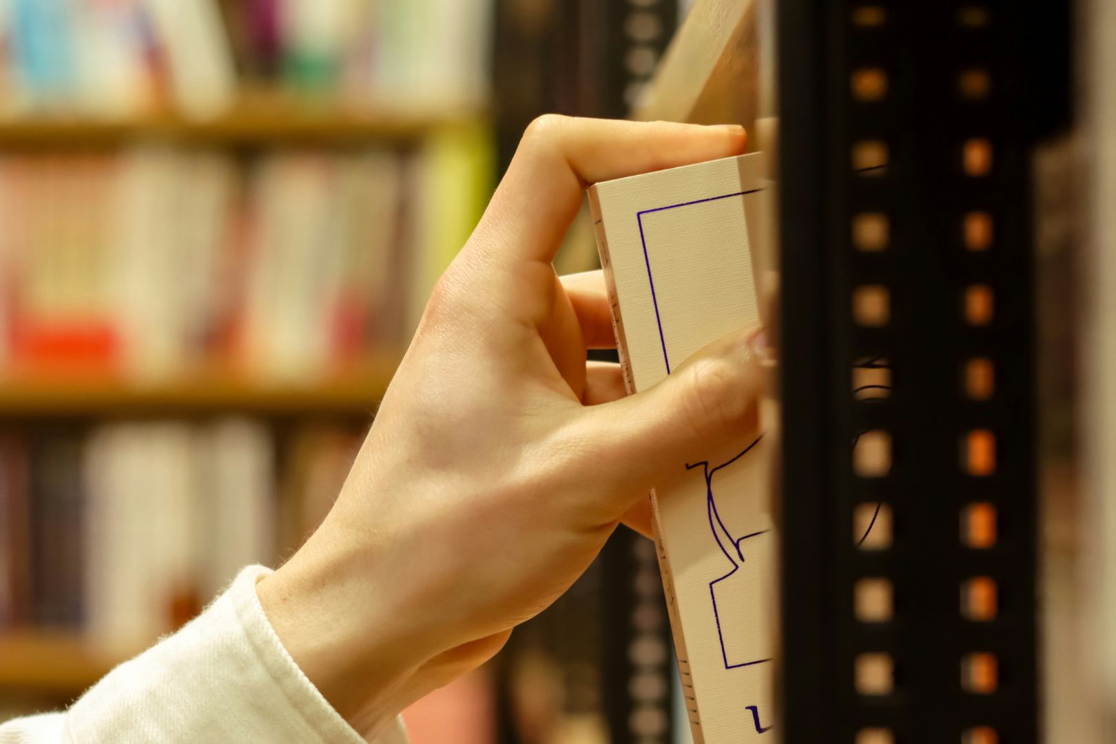 Image of hand pulling book from shelf in library